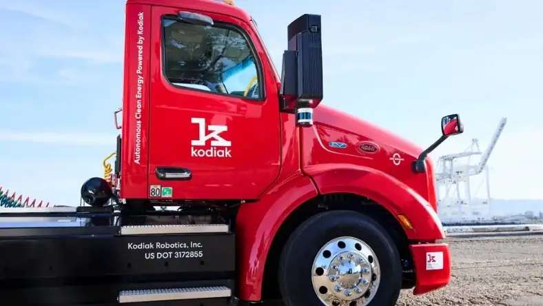 Side view of a red Kodiak AI autonomous truck with roof-mounted sensors and company logo on the door panel