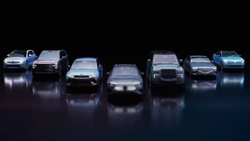 Seven electric vehicles with illuminated headlights and front grilles on a dark reflective studio surface