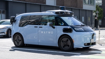 White Waymo driverless vehicle with rooftop sensor array at a city street crossing alongside other traffic